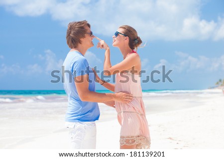 portrait of happy young couple in sunglasses in bright clothes flirting on tropical beach