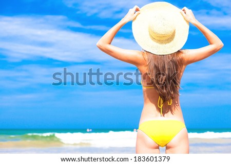 Young fit woman in bikini and straw hat at beach. back view