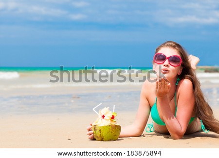 portrait of fit young woman in bikini with coconut on the beach blowing air kiss