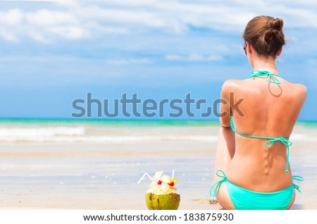 back view of fit young woman in bikini with coconut on the beach