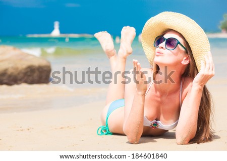 portrait of young woman in sunglasses and straw hat blowing an air kiss on beach