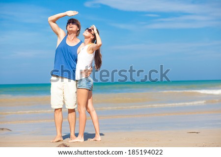 Couple in bright clothes on tropical beach looking at sky