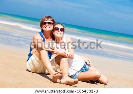 happy young couple in bright clothes in sunglasses sitting on beach. thumbs up