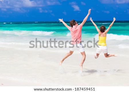 Young couple in bright clothes jumping on the beach