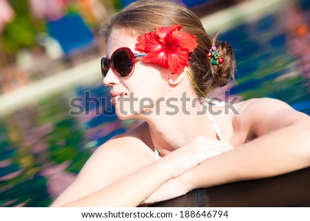 Beautiful young woman in sunglasses with flower in hair smiling in luxury pool