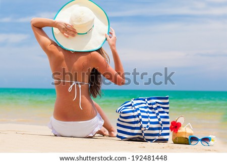 back view of a woman in bikini and straw hat with beach bag and coconut cocktail