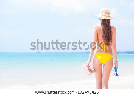 young beautiful woman in yellow bikini and straw sun hat walking on beach. Thailand, Khao Lak