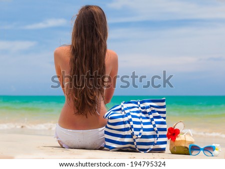 back view of a woman in bikini with beach bag and coconut cocktail