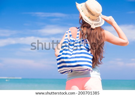 back view of a woman with stripy bag and straw hat at tropical beach