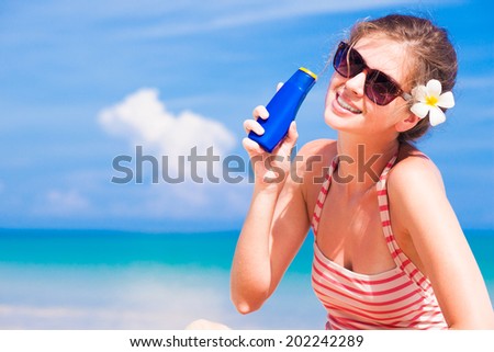 Back view young long haired woman in white shirt and sunglasses with flower in hair sitting on beach