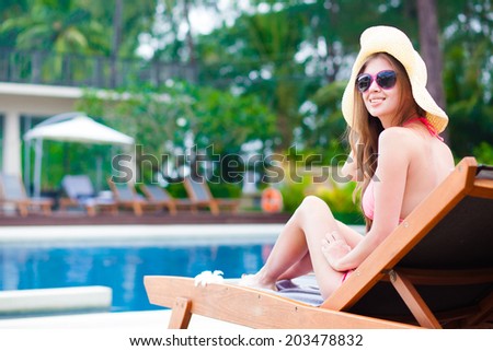 Happy young woman in bikini enjoying her time on chaise-longue luxury pool side