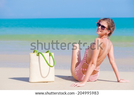 back view of a woman in stripy swimsuit with beach bag at tropical sand beach