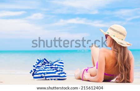 back view of a woman with stripy bag and straw hat sitting on beach