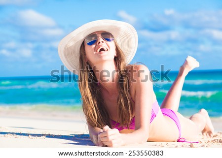 back view of long haired woman in bikini and in a hat on tropical beach