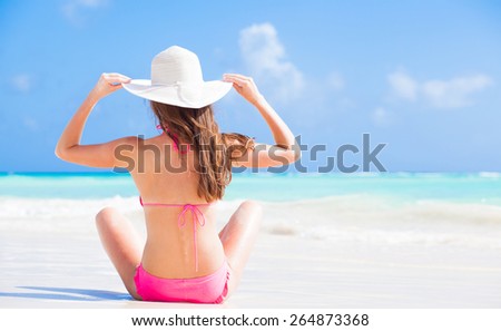 back view of long haired woman in bikini and wearing a hat on tropical beach