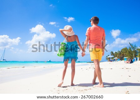 back view of happy romantic young couple holding hands on the beach