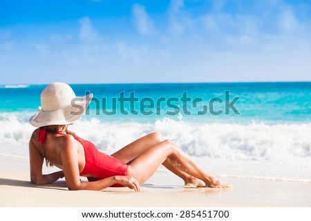 back view of long haired young woman in swimsuit and straw hat on tropical caribbean beach