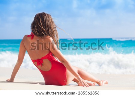 back view of long haired woman in red swimsuit relaxing at beach
