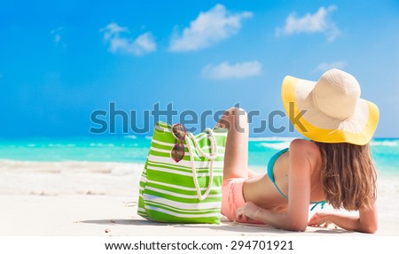 back view of a woman with stripy bag and straw hat lying on beach
