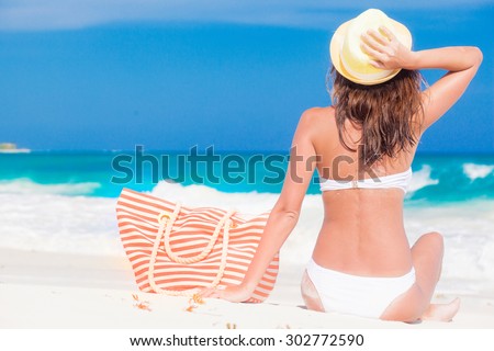 back view of a woman with stripy bag and straw hat lying on beach
