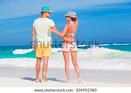 Back view of couple in bright clothes having fun at tropical beach