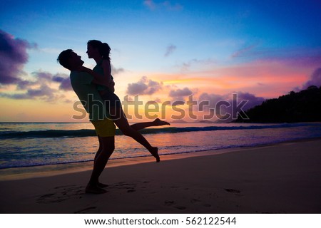 sunset silhouette of young couple in love hugging at beach