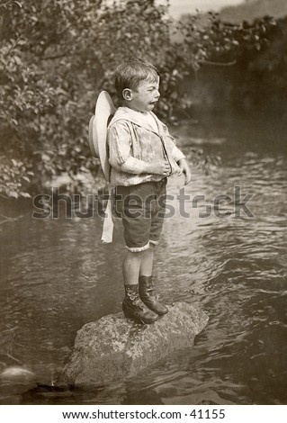 Stranded Cry-Baby - a young boy is stranded on a rock in the middle of a stream, and has a pitiful bawl-baby expression on his face.  A circa 1900, vintage photograph.