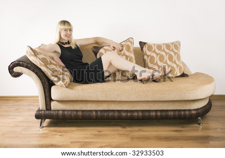 Blond girl sits on the sofa against the background of the white wall