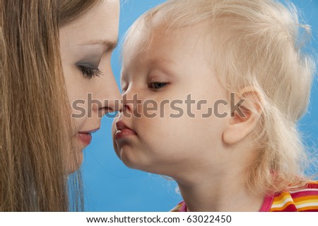 Young and beautiful mother with her sweet little daughter isolated on blue.