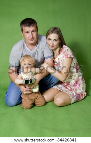 Young European family from three persons - mother, father and son. On a green background.