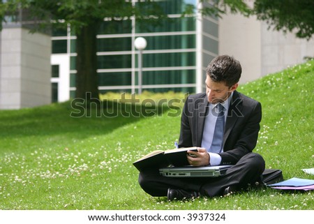 business man with laptop and notebook working in the park in front of office building