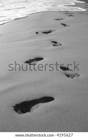 footprints at the beach soon being washed away by a wave - black and white
