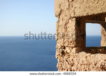 beautiful view on deep blue ocean water through window of an old lookout tower at the coast of majorca