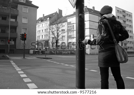 young woman standing in front of red traffic lights pushing the button and waiting for green (black and white image only with traffic lights red)