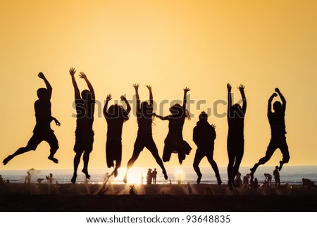 eight young people jumping on a beach in the Netherlands against the setting sun