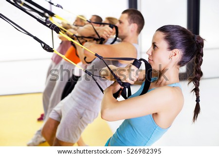 Group of people exercising with hanging fitness straps at the gym.