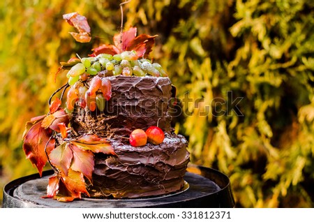 beautiful designer chocolate cake decorated with grapes and orange leaves standing on a wooden wine barrel.
