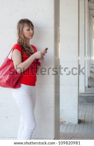 the beautiful young girl costs at columns of a big building with phone in hands