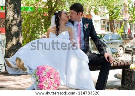 beautiful groom and the bride sit on a bench in park among green foliage