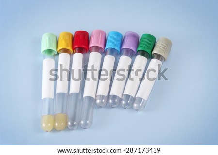 An assortment of Blood Draw Tubes with Rainbow Colored Caps lie on a light blue background.  Labels are plain white.  Medical supplies used by phlebotomists and lab technicians.