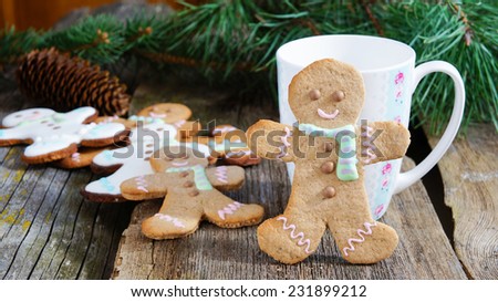 Smiling gingerbread man standing next to tea cup with baking ingredients and additional gingerbread cookies in background. Partially decorated cookies in foreground