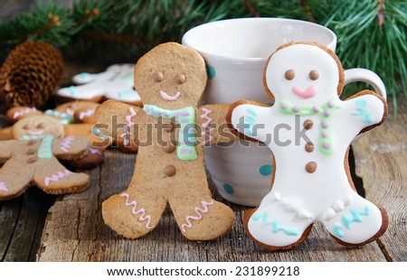 Smiling gingerbread man standing next to tea cup with baking ingredients and additional gingerbread cookies in background. Partially decorated cookies in foreground