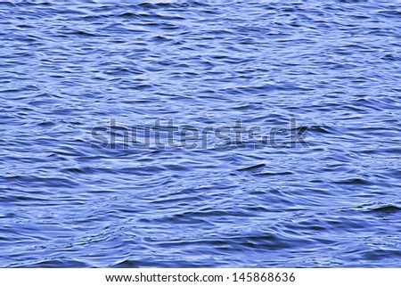 A brilliant blue lake water with small, wind driven waves.
