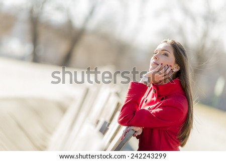 Pretty young woman in red coat by the wooden fence