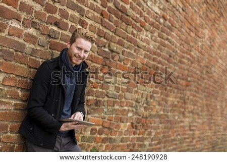 Young man with tablet by the brick wall