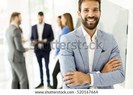 Young businessman standing in the office and other young business people talking in the background