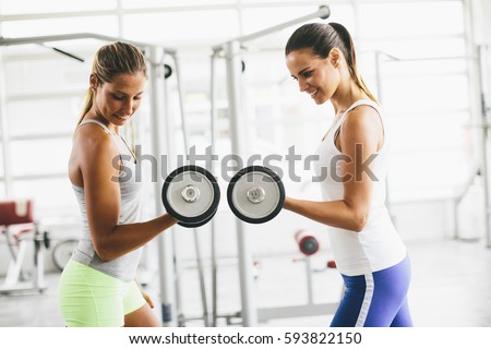 Two pretty young women having dumbbells workout in the gym