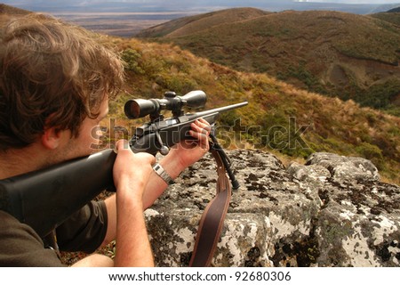 hunter in alpine tussock aiming rifle