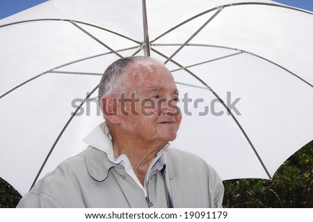 Senior man sitting under an umbrella in the hot sun