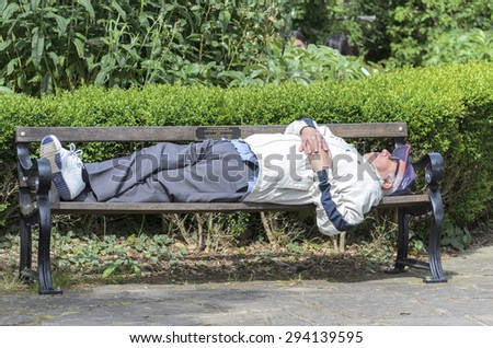 Essex, England. UK 18 June 2015-A homeless man is sleeping on a bench in the park on a summers day.